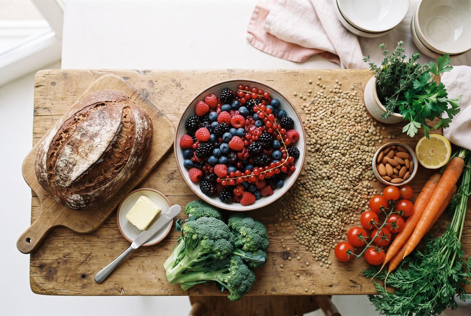Bunte Vielfalt ballaststoffreicher Lebensmittel wie Beeren, Vollkornbrot, Brokkoli und Linsen auf einem Holztisch.